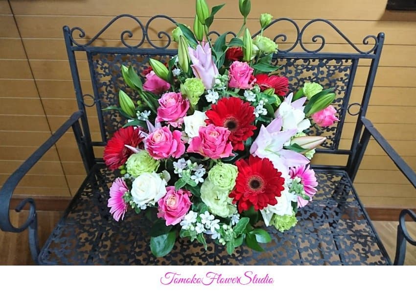 赤いガーベラ、ピンクのバラ、淡いピンクのユリ、淡い黄緑色のバラ、白い小花を散らしたアレンジ。法人様にお届け用。